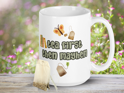 Ceramic Dragon Mug with handle to the right. In light green outlined in black are the words, "tea first then mayhem". Sitting on the word then like a bookshelf are 4 books. Above the words is a yellow butterfly and a tea bag. Below the words is a tea bag.