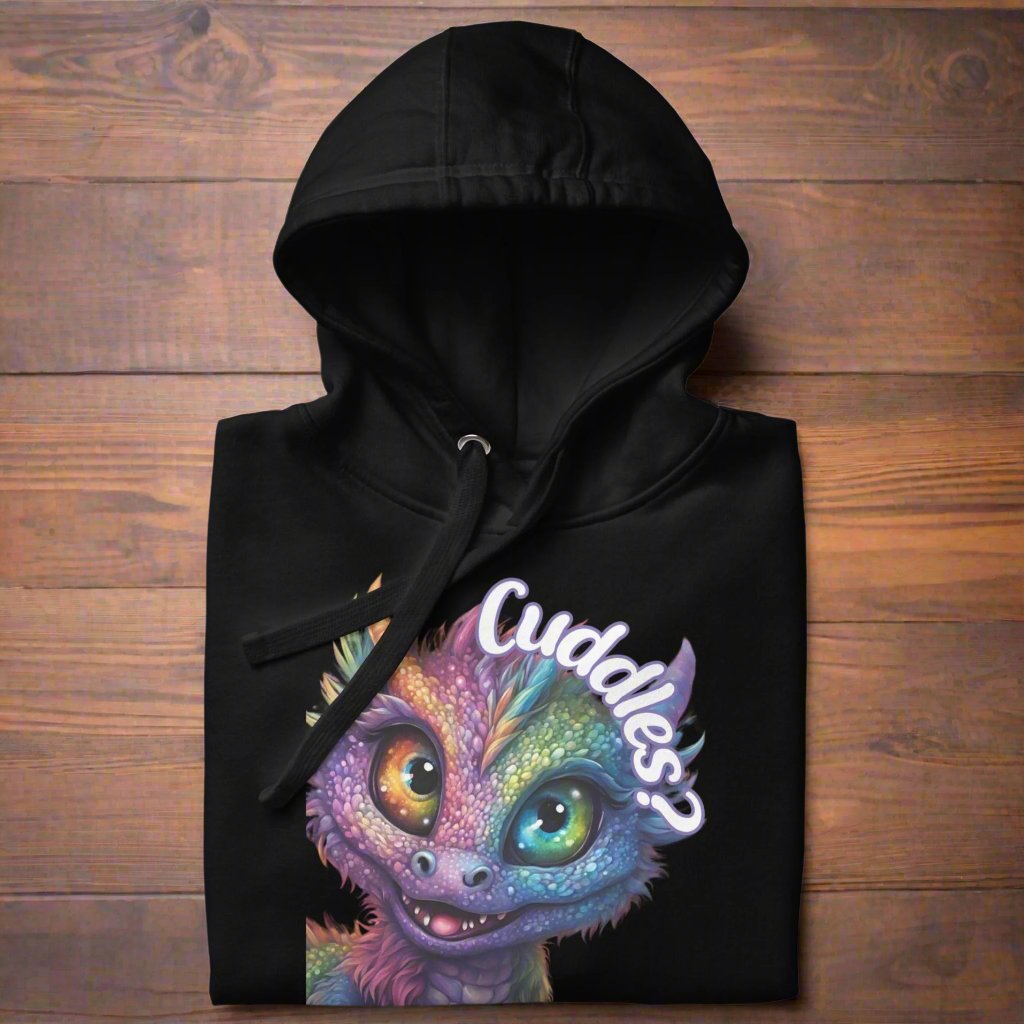 black Women's Hoodie Front View folded with hoodie up on a wooden background. Purple cross eyed baby dragon. Text above dragon circling head "Cuddles?". 