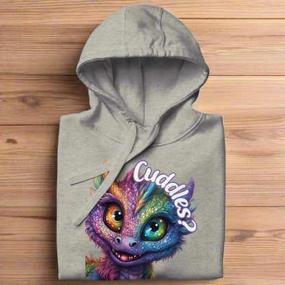 Carbon Grey Women's Hoodie Front View folded on a wooden surface. Purple cross eyed baby dragon. Text above dragon circling head "Cuddles?". 