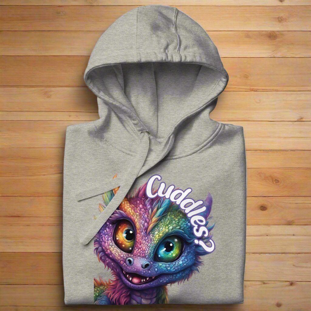 carbon grey Men's Hoodie Front View folded on wooden surface. Purple cross eyed baby dragon. Text above dragon circling head "Cuddles?". 