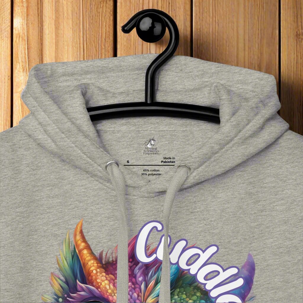 carbon grey Men's Hoodie Front View up close on hanger to show inside tag, collar, hood folded down, and strings coming out of silver toned grommets. Purple cross eyed baby dragon. Text above dragon circling head "Cuddles?". 