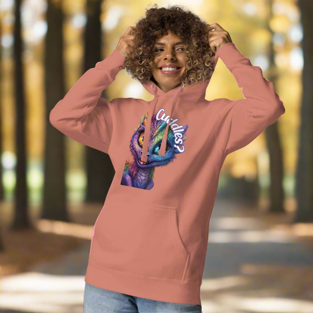 dusty rose Women's Hoodie Front View with hood pulled up. Purple cross eyed baby dragon. Text above dragon circling head "Cuddles?". 