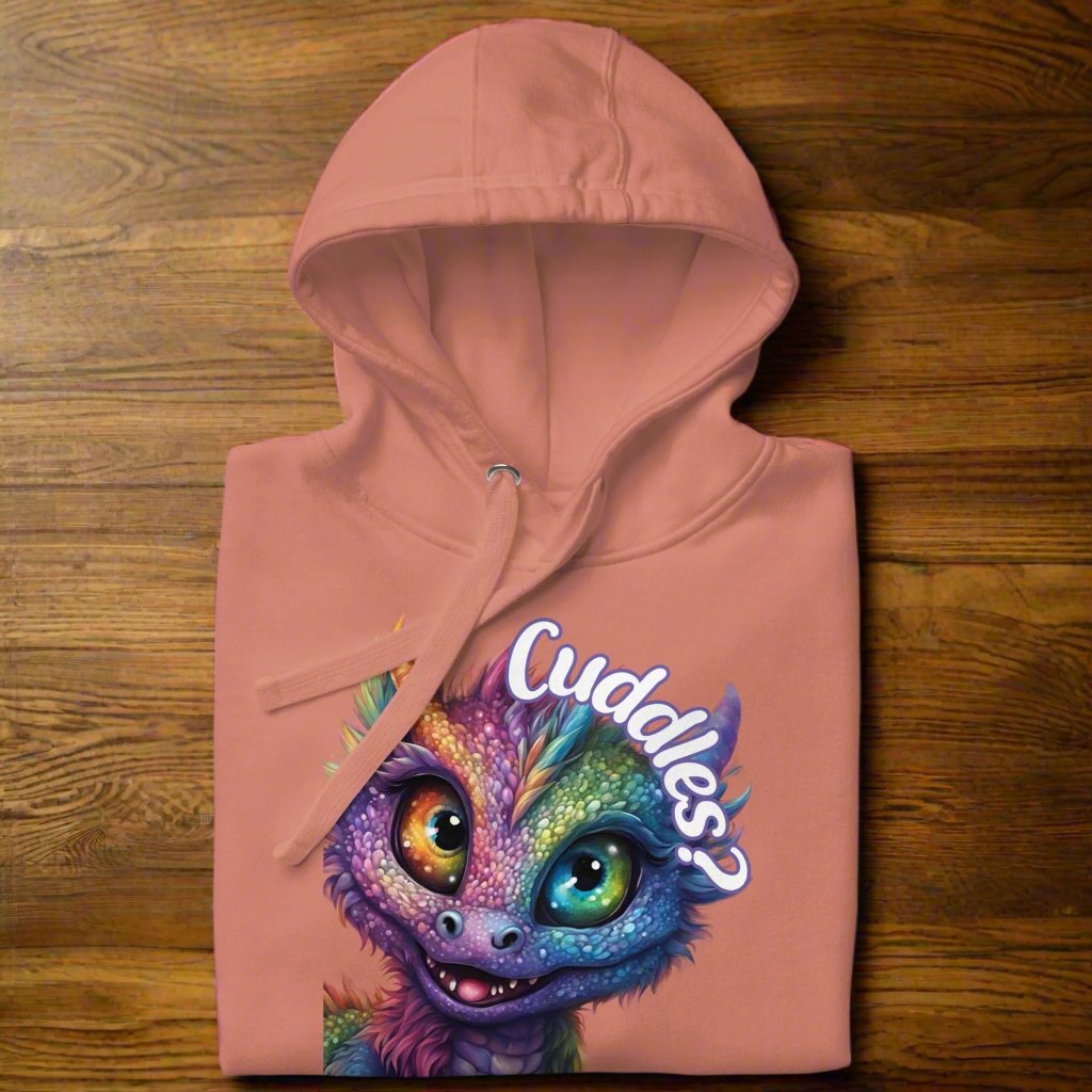 dusty rose Men's Hoodie Front View folded on a wooden counter. Purple cross eyed baby dragon. Text above dragon circling head "Cuddles?". 