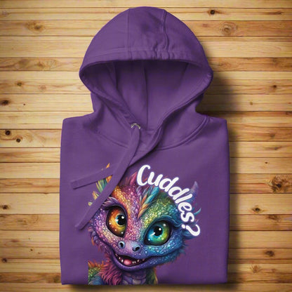 Purple Women's Hoodie Front View folded on a wooden surface with hood up. Purple cross eyed baby dragon. Text above dragon circling head "Cuddles?". 