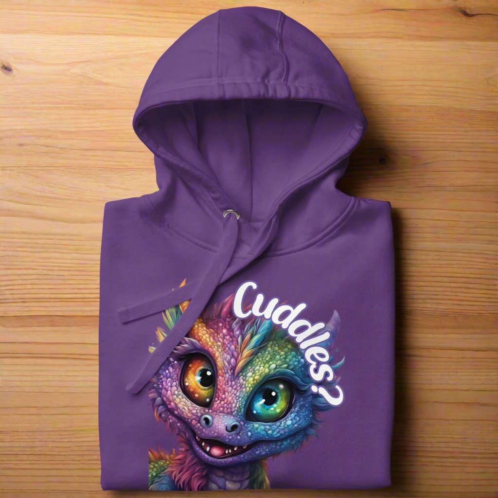 purple Men's Hoodie Front View folded on a wooden counter. Purple cross eyed baby dragon. Text above dragon circling head "Cuddles?". 