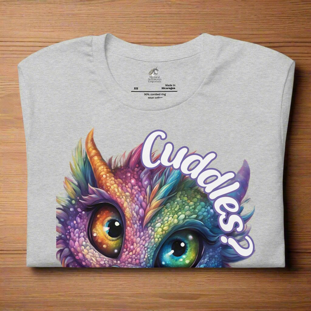 athletic heather Dragon Cuddles Front View Men's T-Shirt folded on a wooden surface. Whimsical purple iridescent  dragon looking up at the word Cuddles? above his head