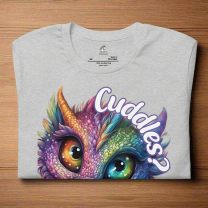 athletic heather Dragon Cuddles Front View Men's T-Shirt folded on a wooden surface. Whimsical purple iridescent  dragon looking up at the word Cuddles? above his head