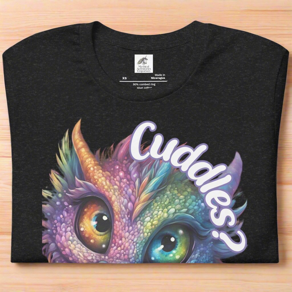 black heather Dragon Cuddles Front View Men's T-Shirt folded on wooden surface. Whimsical purple iridescent  dragon looking up at the word Cuddles? above his head