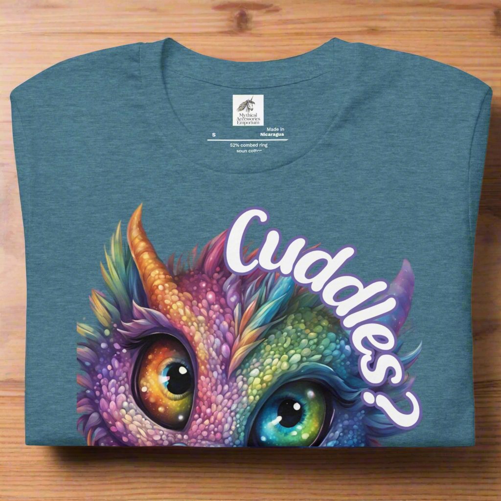 Heather Deep Teal Dragon Cuddles Front View Men's T-Shirt folded on wooden surface. Whimsical purple iridescent  dragon looking up at the word Cuddles? above his head