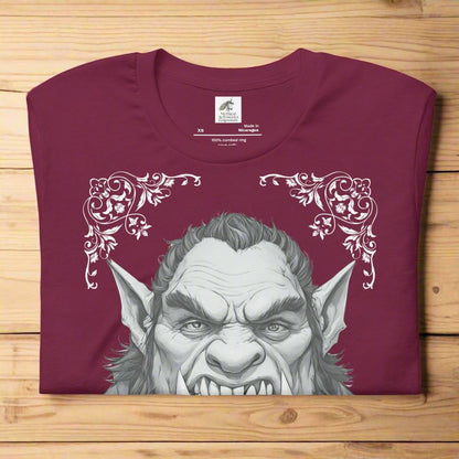 Men's maroon Orc T-Shirt Front View folded on wooden surface. Orc with tusks and pointed ears. Troll TShirt, Giant TShirt, Ogre Shirt