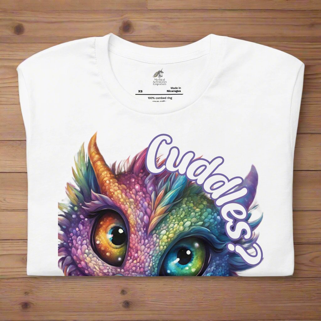 white Dragon Cuddles Front View Men's T-Shirt folded on a wooden surface. Whimsical purple iridescent  dragon looking up at the word Cuddles? above his head