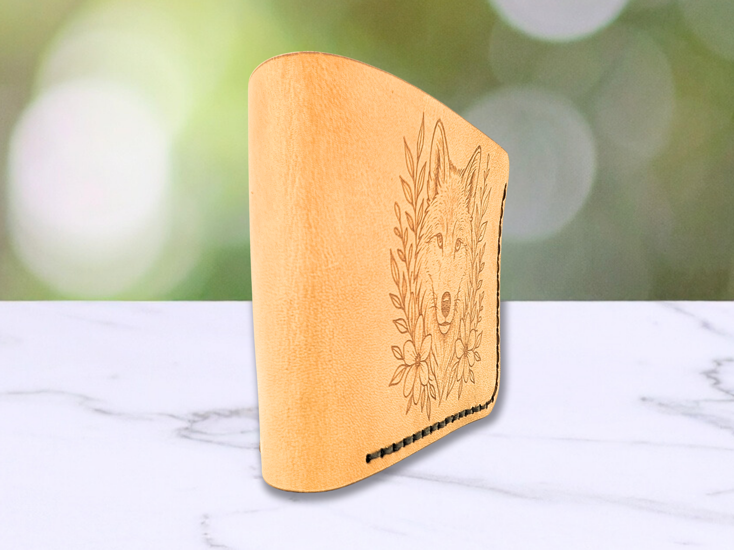 Bi fold beg tan leather wallet with laser engraved wolf head. Wallet is standing on its edge and angled in the photo. You see the folded edge of the wallet.