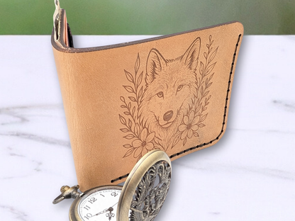 handmade leather wallet with engraved wolf head surrounded by vines and flowers. Wallet is standing up and opened from the back. You can see the folded edge and the front of the wallet. Cash is sticking up out of the cash compartment. You can see the dark edges of the veg tan leather.