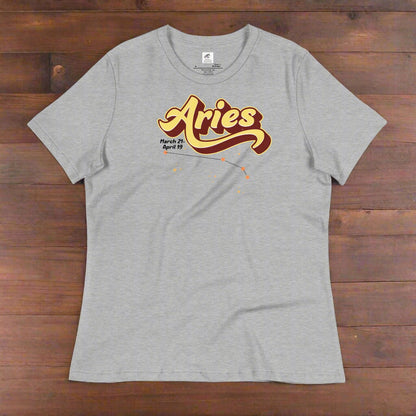 Aries Tee laying flat on a wooden counter, athletic heather (grey). On the top is the word Aries in light yellow lined with maroon. Under the A are the dates March 21-April 19. Below his is the constellation Aries in bright yellow orange stars connected with a black line. Aries constellation zodiac astrology sign.
