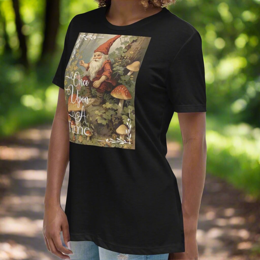 Model front view tilted to the side wearing a relaxed women's black graphic t-shirt. Graphic is Once Upon A Time with a vintage fairy tale artwork of a gnome sitting in a forest amidst mushrooms.