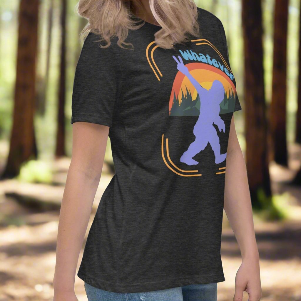 Dark Grey Sasquatch Women's T-Shirt model facing right. Big Foot in periwinkle against a rainbow and mountains showing a peace sign with text Whatever. Bigfoot Yeti Women's Tee