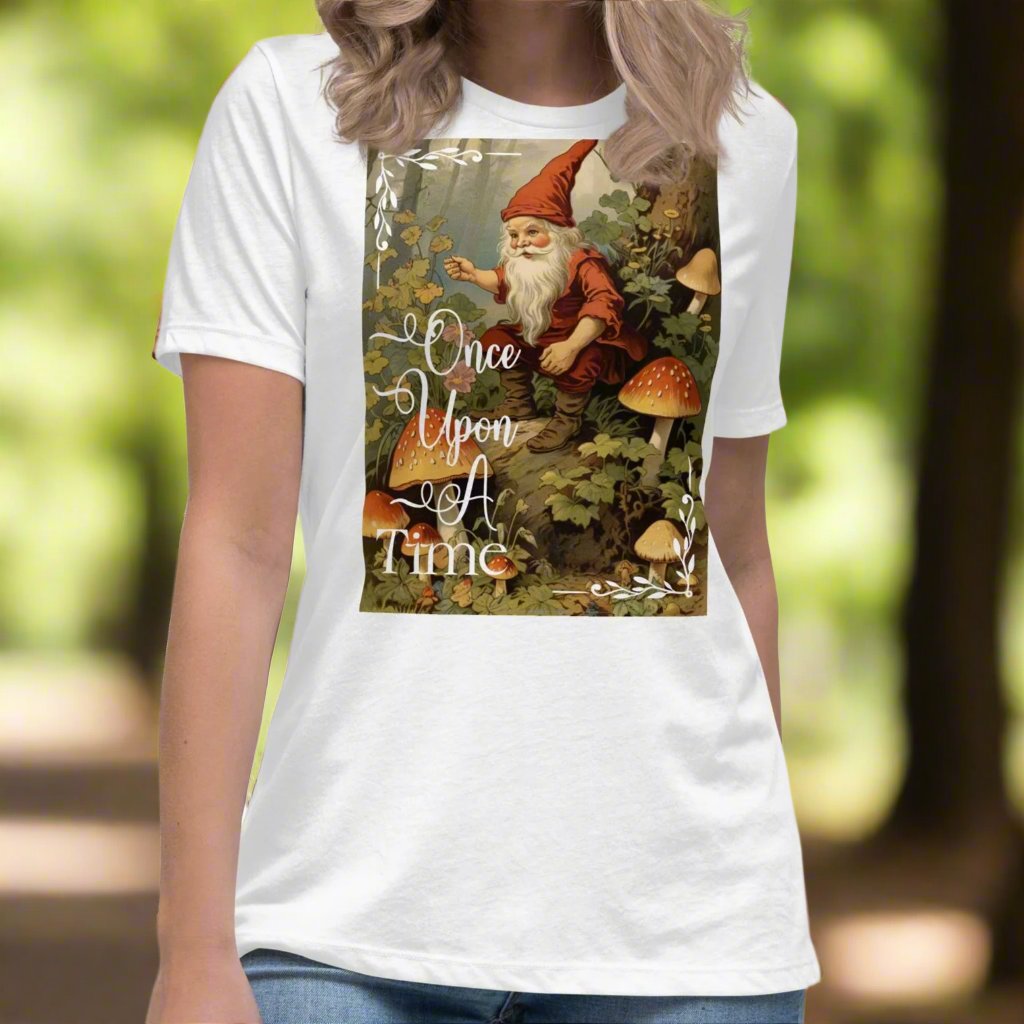 Front view of model wearing a relaxed women's graphic t-shirt in white. Vintage image from a 1800s fairy tale of a gnome with a long white bear, red hat, gesturing with a pipe sitting in a forest surrounded by mushrooms.