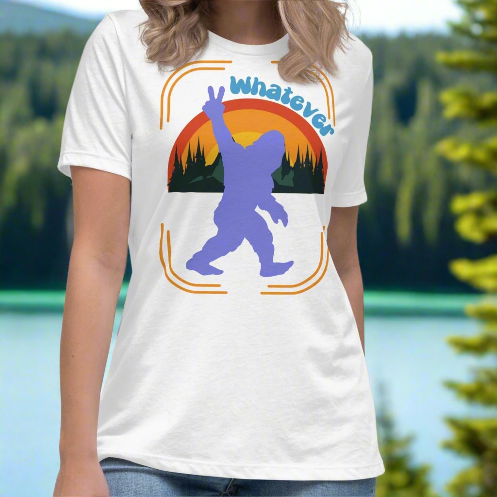 white Sasquatch Women's T-Shirt on model facing forward. Big Foot in periwinkle against a rainbow and mountains showing a peace sign with text Whatever. Bigfoot Yeti Women's Tee