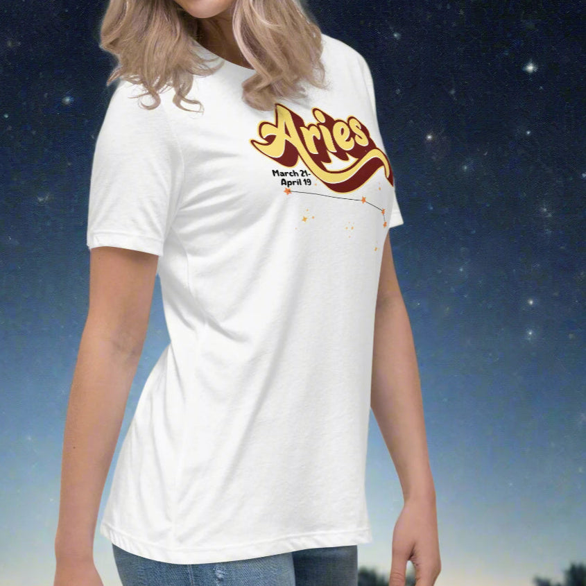 Woman wearing a white t-shirt facing slightly to the right. Arm is moved back to show the side seam on the shirt. On the top is the word Aries in light yellow lined with maroon. Under the A are the dates March 21-April 19. Below his is the constellation Aries in bright yellow orange stars connected with a black line. Aries constellation zodiac astrology sign.
